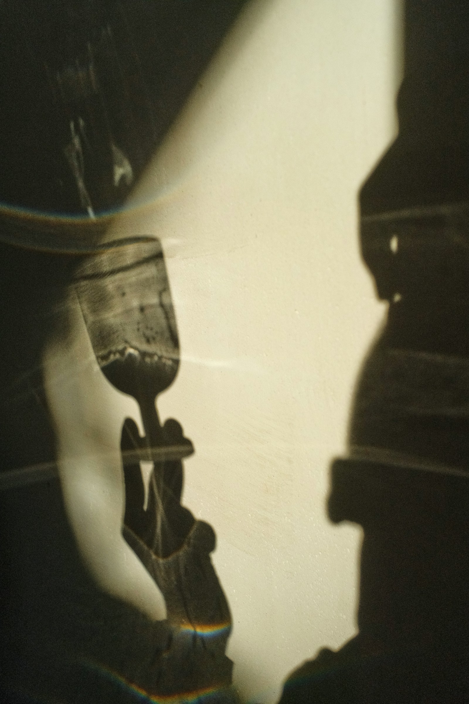 A hand and glass casting warm shadows on a wall